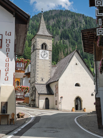 Historic Clock Tower In Canazei Village Amidst Alpine Buildings and Mountain Background, Italy.