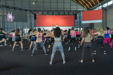 Fitness Workout in Gym: People doing Exercises in Class with Music and Teacher on Stage.