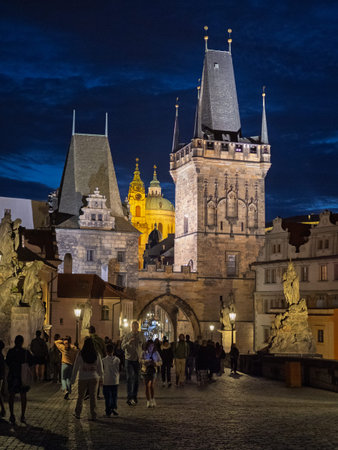 Pedestrians Crossing Charles Bridge Under Lesser Town Towers And Night Sky, Prague, Czech Republic.