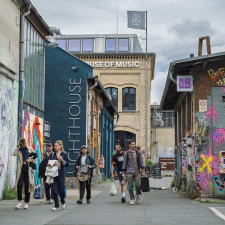 Music Band Members Carrying Equipment Between Graffiti Covered Walls And Old Buildings in Berlin.