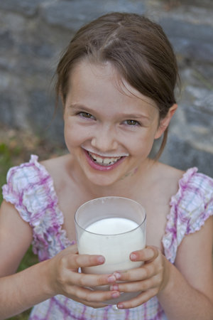 seven year old girl is drinking milk outside in the summerの写真素材