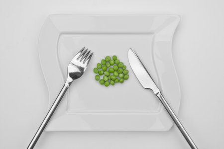 a bunch of peas on a white plate with fork and knifeの写真素材