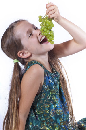 eight year old girl eating freshly picked grapes from the gardenの写真素材