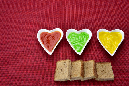 white heart shape bowl with sauces with cut breads on red background.の写真素材