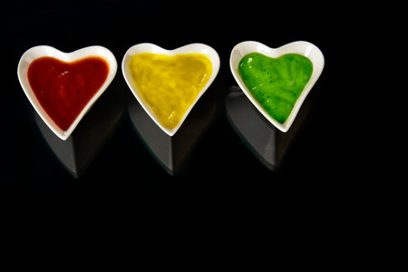 White porcelain heart shape bowl with colorful sauces on black background.の写真素材