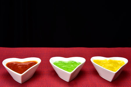 white heart shape bowl with sauces with cut breads on red background.