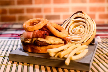 hamburger sandwich with open brioche bread cream cheese fries bacon sauces on the table on blurred backgroundの写真素材