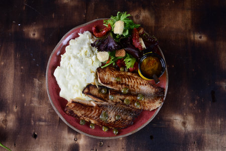 plate with piece of meat roasted fish with bacon vegetable salad and mustard sauceの写真素材