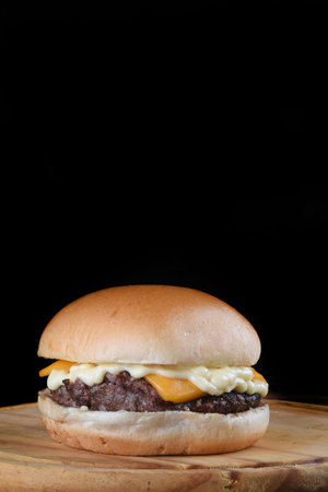 beef burger sandwich with bacon cheese salad and soft egg bun, side view on wooden table isolated on black backgroundの写真素材