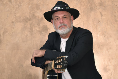portrait adult man with white beard and bald head posing with a guitar.