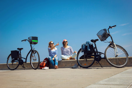 Two young women sitting on the beach with bicycles