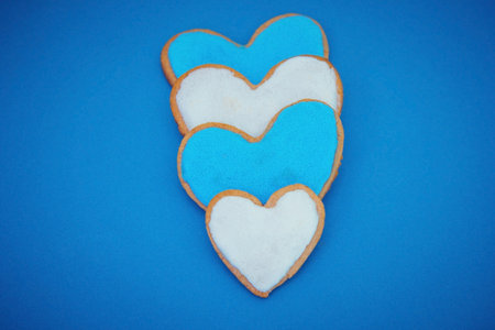 Four blue and white homemade heart shape cookies on blue backgroundの写真素材
