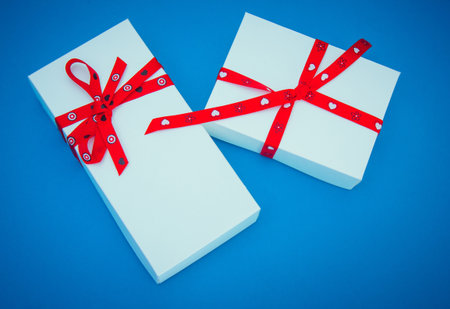 Two white gift boxes with red ribbons on blue backgroundの写真素材