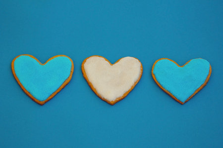 Three blue and white homemade heart shape cookies in a row on blue backgroundの写真素材