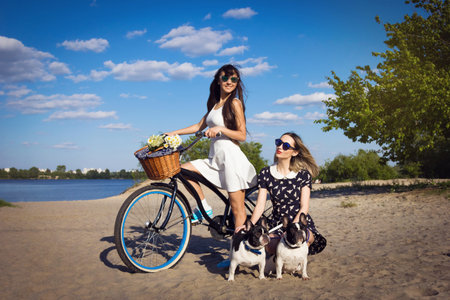 Two beautiful young women on the beach with bicycle and french bulldogsの写真素材