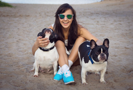 Beautiful young woman on the beach with two french bulldogsの写真素材