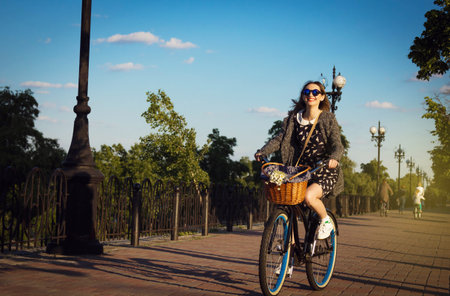 Beautiful young woman ride a cruiser bicycle with flowers in basketの写真素材