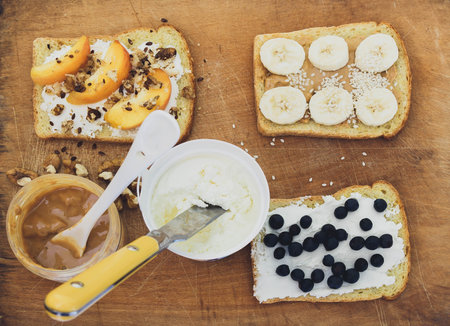 Toasts with peanut butter, cheese and fresh fruits on wooden backgroundの写真素材