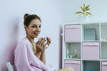 Beautiful young woman with cup in hands and pink plaid on shouldes in beauty salonの写真素材