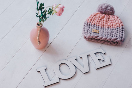 Pink knitted hat lying on the white wooden floor with rose and wooden LOVE signの写真素材