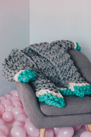 Grey knitted merino wool cardigan lying on grey arm-chair, Pink balloons on the floorの写真素材