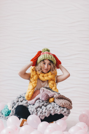 Beautiful young woman sitting on the floor with a lot of knitted colorful clothingの写真素材