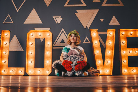 Beautiful young woman sitting on the floor with knitted clothing between electric bulbsの写真素材