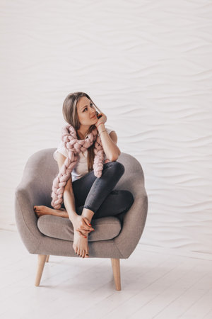 Beautiful young woman sitting in gry arm-cahir with knitted merino wool scarfの写真素材