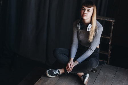 Young girl sitting on skateboard with headphones in loft appartmentの写真素材