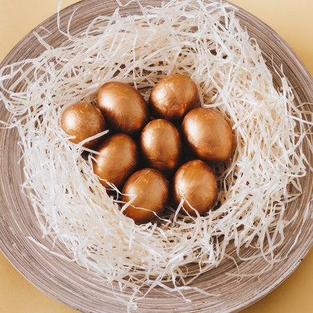 Golden Easter eggs in the straw on the round wooden plateの写真素材
