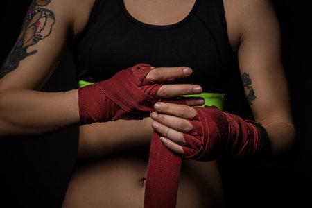 Woman wrapping hands with red boxing wraps in dark room. Close-up shotの写真素材