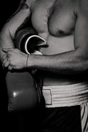 Boxer man putting on boxing gloves in dark room. Black and white close-up shot