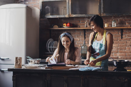 Young woman with her little sister cooking holiday pie in the kitchenの写真素材