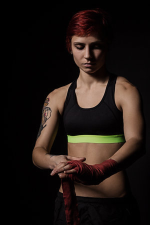 Woman is wrapping hands with red boxing wraps in dark roomの写真素材