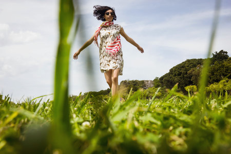 Beautiful young woman in beautiful dress dancing in the green grass fieldの写真素材