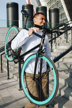 Mixed race smiling hipster man carrying bicycle on shoulder in the city