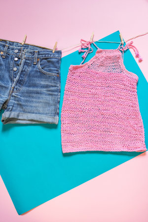 Knitted pink top and jeans shorts on blue background. Top shot