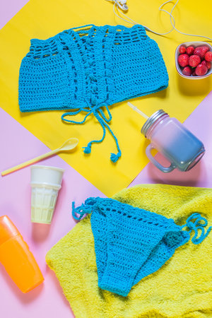 Knitted blue swimsuit on pink and yellow background. Top shot