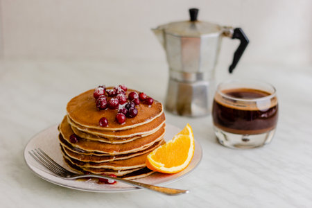 Stack of pancakes with cranberries and maple syrup and coffee on marble background