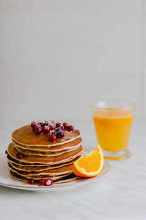 Stack of pancakes with cranberries and maple syrup and orange juice on marble backgroundの写真素材