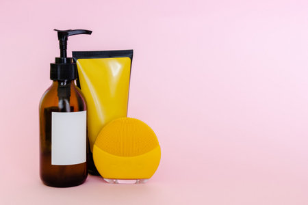 Cosmetic bottle and container with blank labels for branding mock-up and yellow cleansing brush on pink backgroundの写真素材