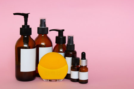 Cosmetic bottles with blank labels for branding mock-up and yellow cleansing brush on pink backgroundの写真素材