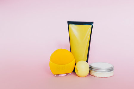 Cosmetic bottle and containers with blank labels for branding mock-up and yellow cleansing brush on pink backgroundの写真素材