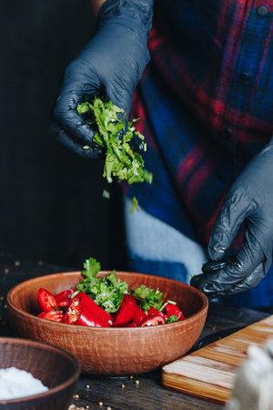 Woman hands in black gloves blending red hot chili peppers and parsley in a bowlの写真素材