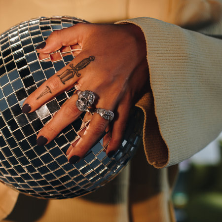 Close up of tattooed woman hand with silver rings holding disco ballの写真素材
