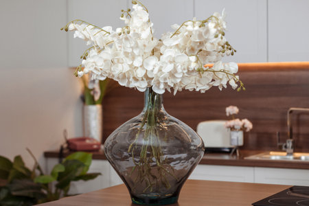 White Orchids flowers branches in glass vase on wooden tableの写真素材