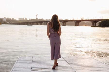 Back view of young woman with beautiful long hair standing on the pierの写真素材