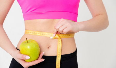Fit woman measuring her waist and holding green appleの写真素材