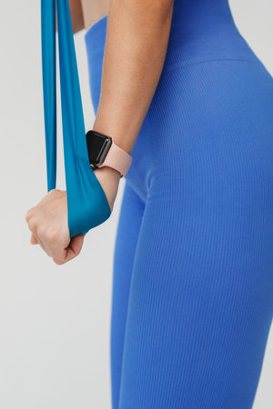 Young fit women wearing blue leggings trains arm muscles with fitness elastic band isolated on white backgroundの写真素材