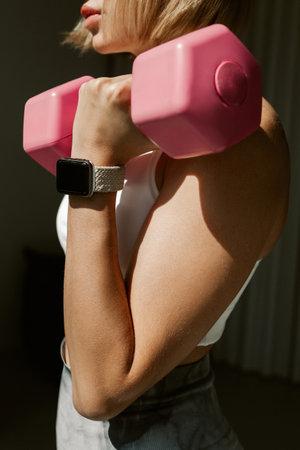Crop image of a beautiful young fit caucasian woman exercising with pink dumbbells indoorsの写真素材